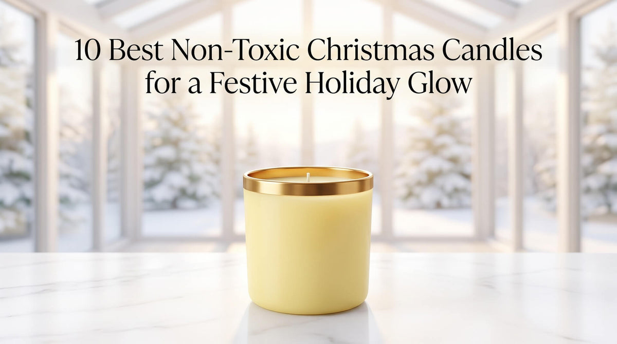 A pale yellow candle with a metallic gold rim positioned on a white marble table in a bright room with blurred snowy trees outside.