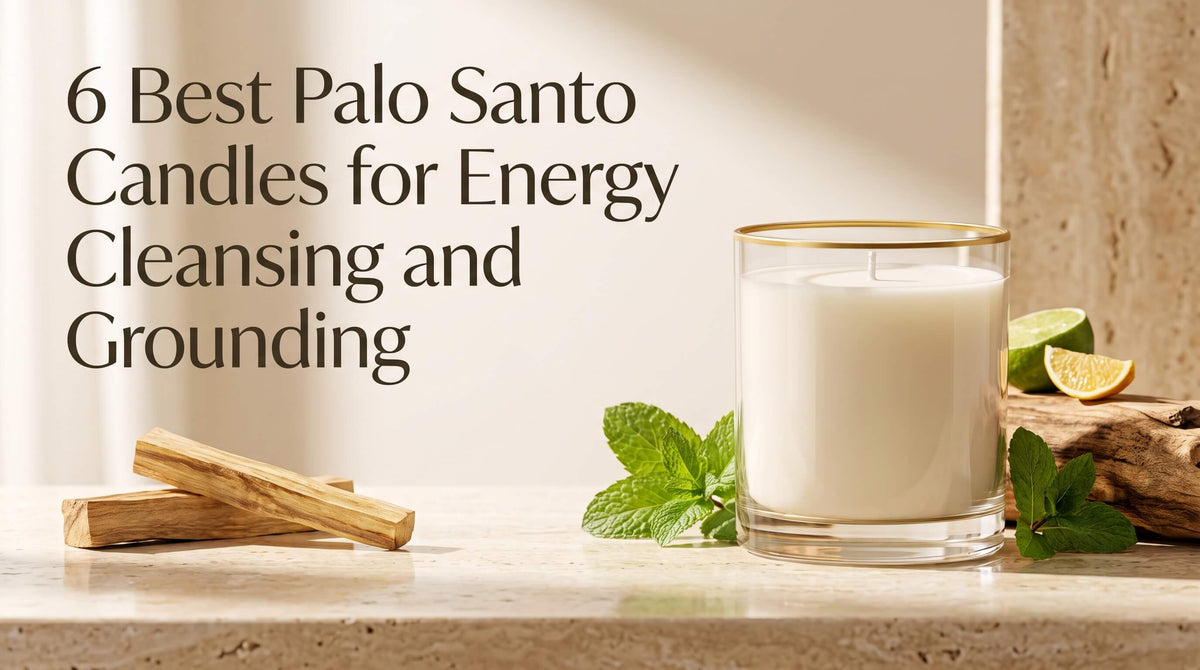 A white unlit candle in a gold-rimmed clear glass jar placed on a beige marble surface beside Palo Santo wood sticks, fresh mint leaves, and lime slices.