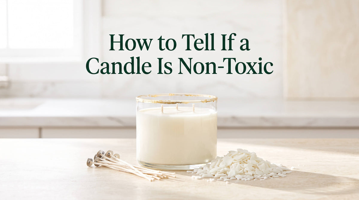 A white three-wick candle in a gold-rimmed glass jar sitting on a counter beside a pile of wax flakes and unattached wicks.