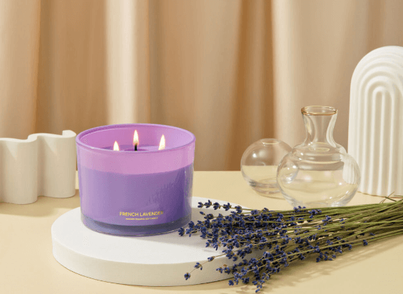 A photo of the 96NORTH French Lavender three-wick long-lasting candle on a table next to sprigs of lavender and glass receptacles.